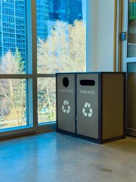 Recycling bins placed by a large window with a view of trees and city build.. 库存照片