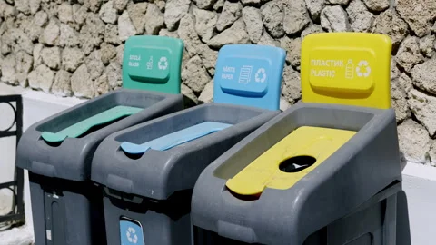 Recycling bins in urban setting, featuring blue, green, and yellow lids for Stock Footage 312741392