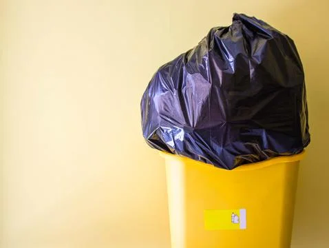 Recycling yellow bin with black bag full of plastic. Free copy space. Concept Stock Photos