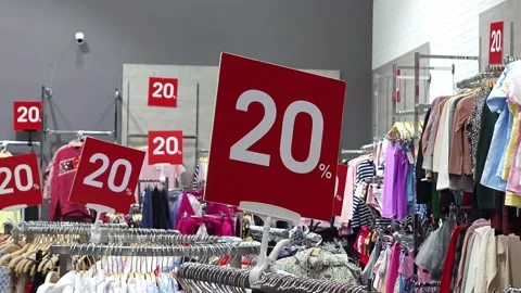 Red 20% discount sign displayed in a fashion store with clothing racks Stock Footage 286906154