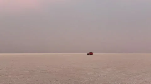 Red 4x4 car driving across a vast and minimalist salt desert landscape in Vídeo Stock 345994563
