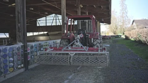 Red agricultural tractor with a cage roller leaving an equestrian riding hall Stock-Footage 332116232