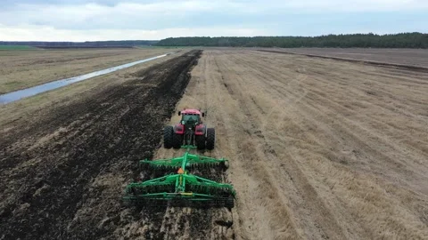 A red agricultural tractor pulls a plow in a farm field Stock Footage 126282530