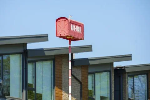 Red air mail box on pole against modern buildings and blue sky Stock Photos