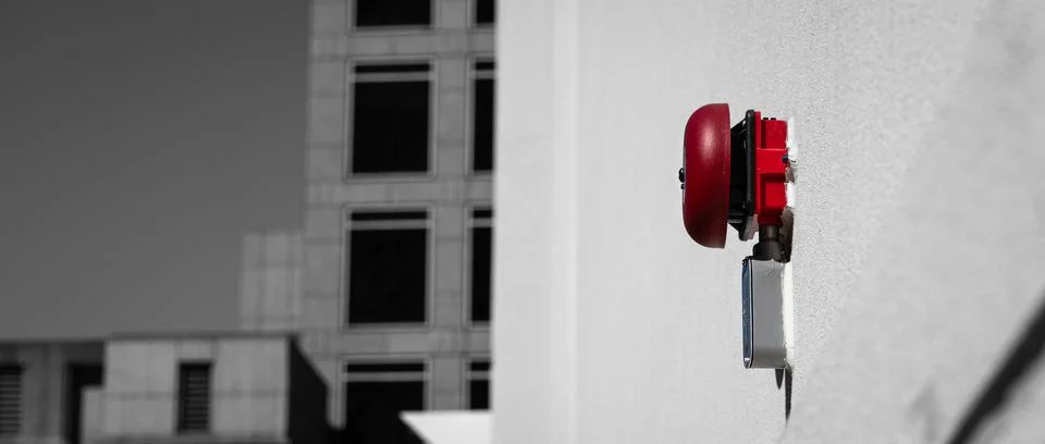 Red alarm bell on white wall with out of focus buildings in background and ne Stock Photos