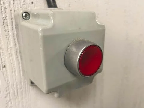 Red alarm button in a gray case. the alarm is connected with a black cable to Stock Photos