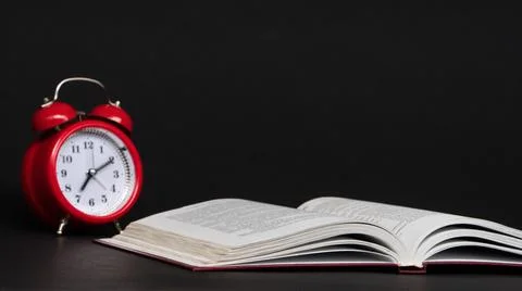 Red alarm clock and open book on black background, isolated. back to school Stock Photos