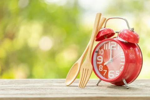 Red alarm clock, Fork, and spoon on wooden table with green outdoor nature .. Stock Photos
