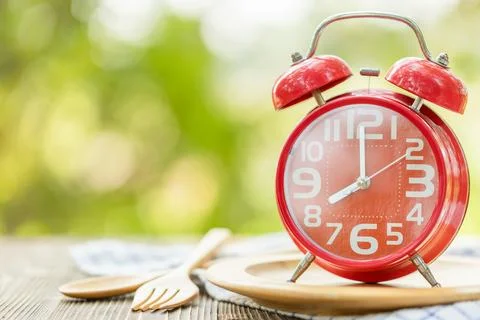 Red alarm clock, Fork, and spoon on wooden table with green outdoor nature .. Stock Photos