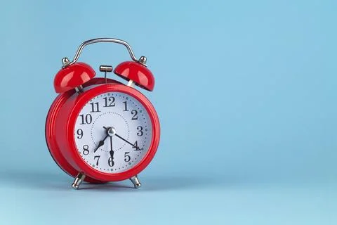 Red alarm clock on a light blue background. It's 7:30 o'clock on the clock. Stock Photos