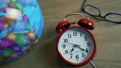 Red alarm clock next to a globe and glasses on a wooden surface Stock Footage 316745405