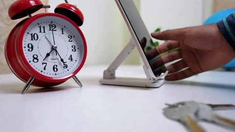 Red alarm clock next to a smartphone on a stand, with a hand typing Stock Footage 317131680