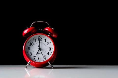 Red alarm clock on a white table with arrows at seven o'clock Stock Photos