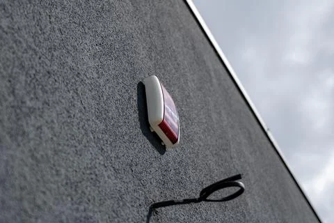 A red alarm system is mounted on a gray wall, with a dark wire hanging down.. Fotos de archivo