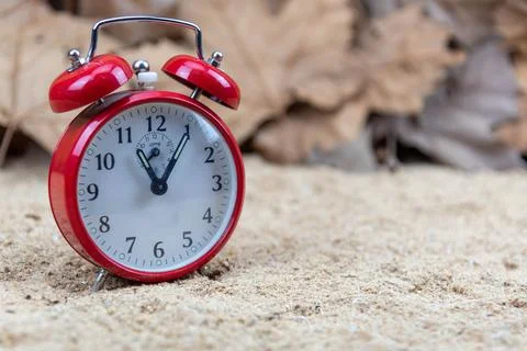 Red analog clock and maple leaves in the background Stock Photos