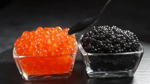 Red and black caviar in two identical transparent glass bowls on a black Video stock 123411081
