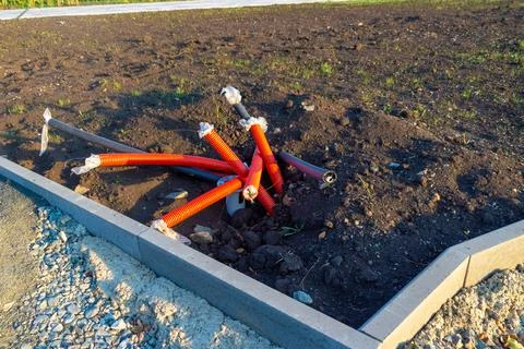 Red and black protective cable corrugations sticking out of the ground around Stock Photos