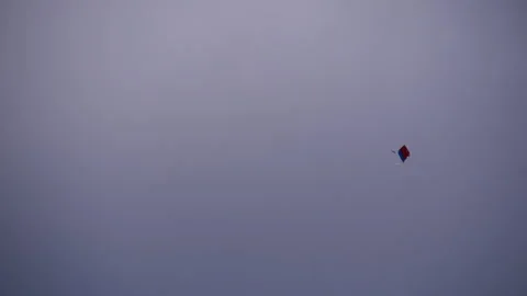 A red and blue kite flying down and up slowly in a white sky Stock Footage 258537352