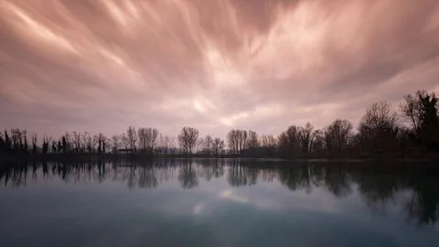 A red and cloudy sky reflected in the water of a lake at sunset time Stock Photos