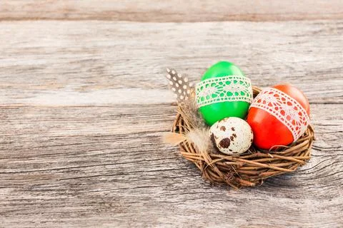 Red and green Easter eggs decorated with lace in small decorative nest Stock Photos