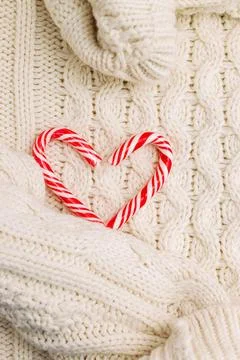 A red and white candy cane shaped into a heart rests on a warm knitted sweate Stock Photos