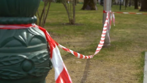 Red and white caution tape tied to columns in city park sways on the wind Stock Footage 106241270