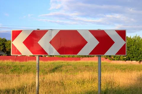 Red and white chevron directional road sign on posts with field Stock Photos