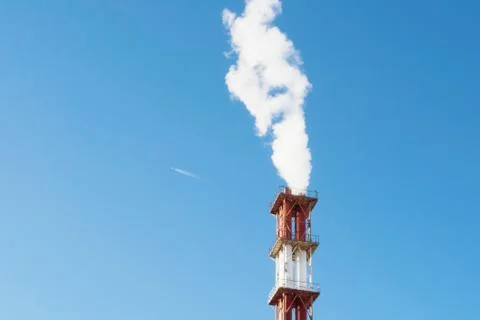 Red and white chimney with a cloud of white smoke against blue clear sky. A f Stock Photos
