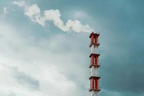 Red and white chimney with a cloud of white smoke against blue gray dramatic  Foto stock