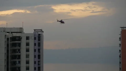 A red and white colored helocopter or chopper flying between two huge buildings Stock Footage 258717284