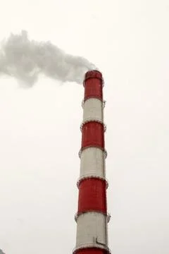 Red and white colored large towering industrial chimney emits smoke into the  Stock Photos