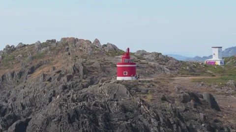 A red and white Faro de Punta Robaleira lighthouse stands on rugged rocky cliffs Stock Footage 346717760