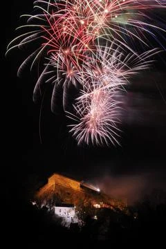 Red and white firework shapes light up the sky above a building at night, New Stock Photos