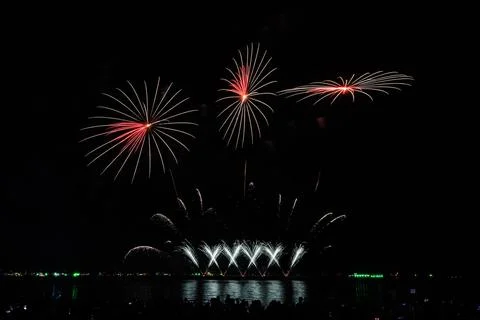 Red And White Fireworks Exploding Over Waterfront Ocean Bay During Night Fe.. Photos