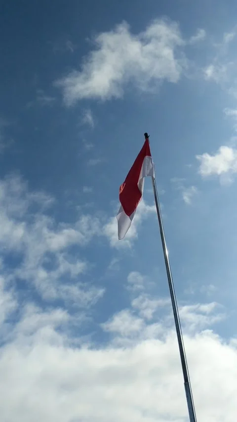 A red and white flag fluttering vertically under a blue sky Stock Footage 304015517