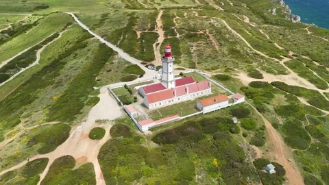 Red and white lighthouse at Cabo Espichel surrounded by green fields Stock Footage 310562663