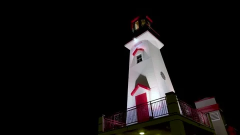 Red and white lighthouse lit up at night against dark black sky with rotating Stock Footage 332103372