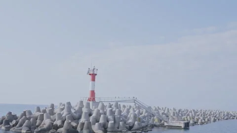 Red and white lighthouse located on shore with stones barriers of sea in island Video stock 255840214