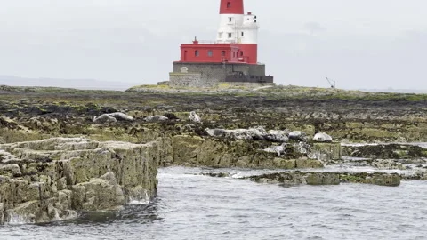 Red and white lighthouse on rocky tidal shore Stock Footage 336545874