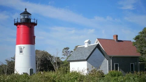 A red and white lighthouse stands on the coast under blue skies Stock Footage 312680882