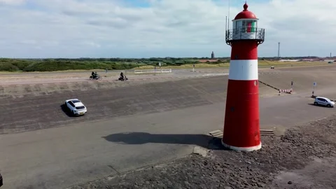 A red and white lighthouse stands on a rocky coastal area Видео 316783385