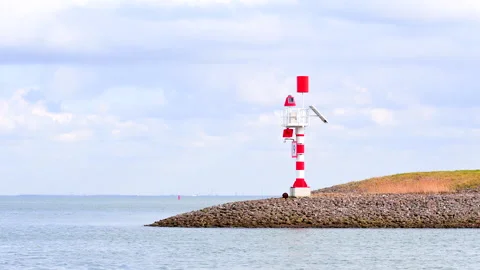 A red and white navigational lighthouse stands on a rocky breakwater Stock Footage 322693908