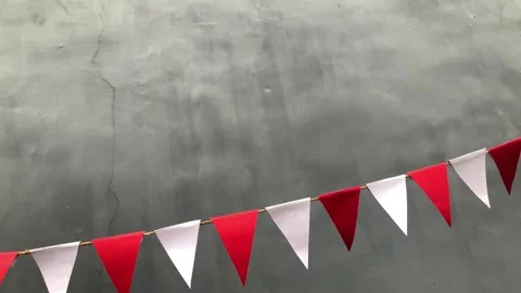 Red and white triangular bunting flags hang against a gray background 動画素材 312499634