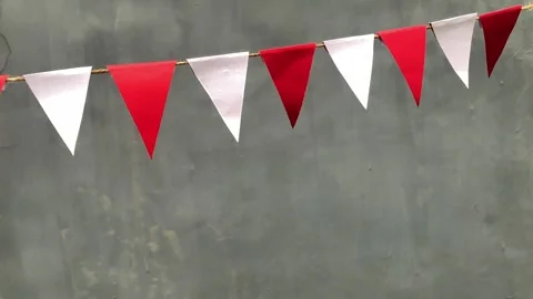 Red and white triangular bunting flags hang against a gray background 動画素材 312499636