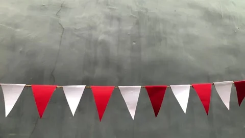 Red and white triangular bunting flags hang against a gray background 動画素材 312499637