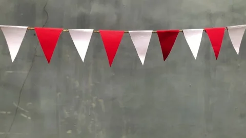 Red and white triangular bunting flags hang against a gray background 動画素材 312499638