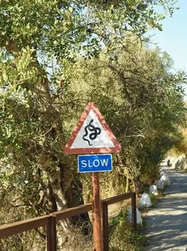 A red and white triangular slow sign featuring a snail symbol by a rural r... Stock Photos