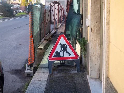 Red and white triangular warning sign indicating men at work stands on a side Stock Photos