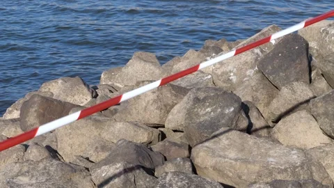 Red and white warning tape over a rocky riverbank close-up shot Vidéo 343547616
