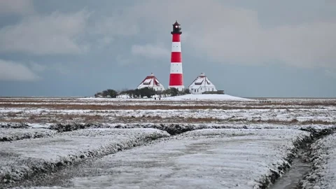 Red-and-white Westerhever lighthouse in snow-covered coast. 스톡 동영상 325845278